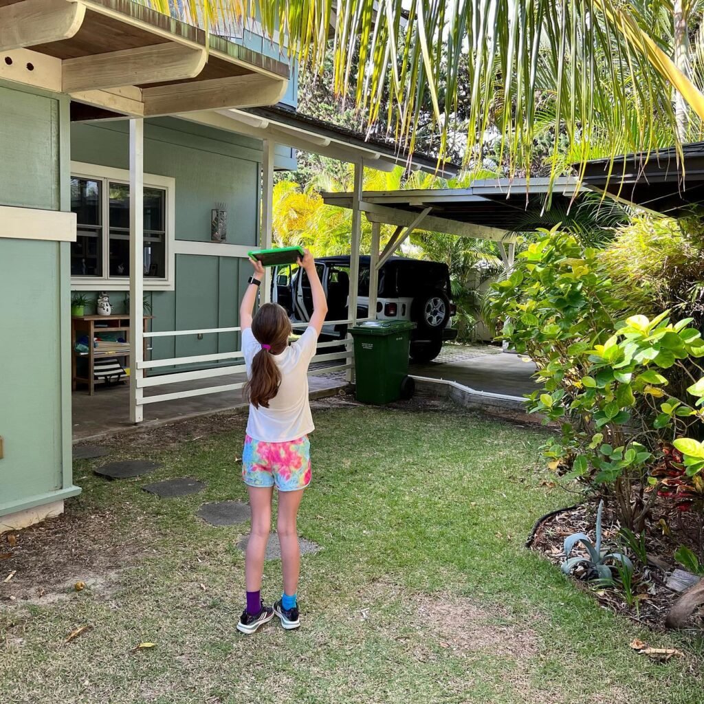 Person practicing yoga under a palm tree at a cabin with a green lawn and car parked on a concrete pad.
