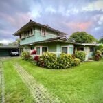 Diamond Head A charming two-story house with a green lawn, colorful flowers, and a carport under a cloudy sky.