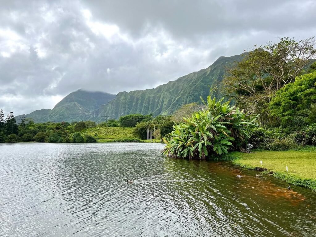 A tranquil lake surrounded by lush greenery and mountains with a dramatic overcast sky above.
