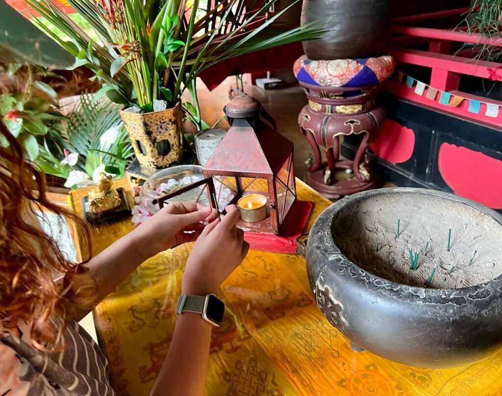 A traveler lights a candle on a temple altar spread with yellow cloth.