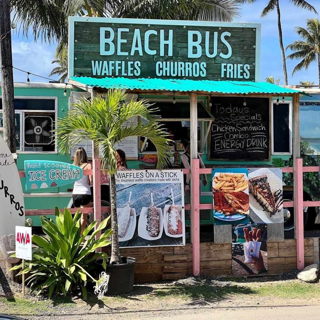 A coastal food stand called Beach Bus with a teal roof and menu items including waffles, churros, and fries set against palm trees.