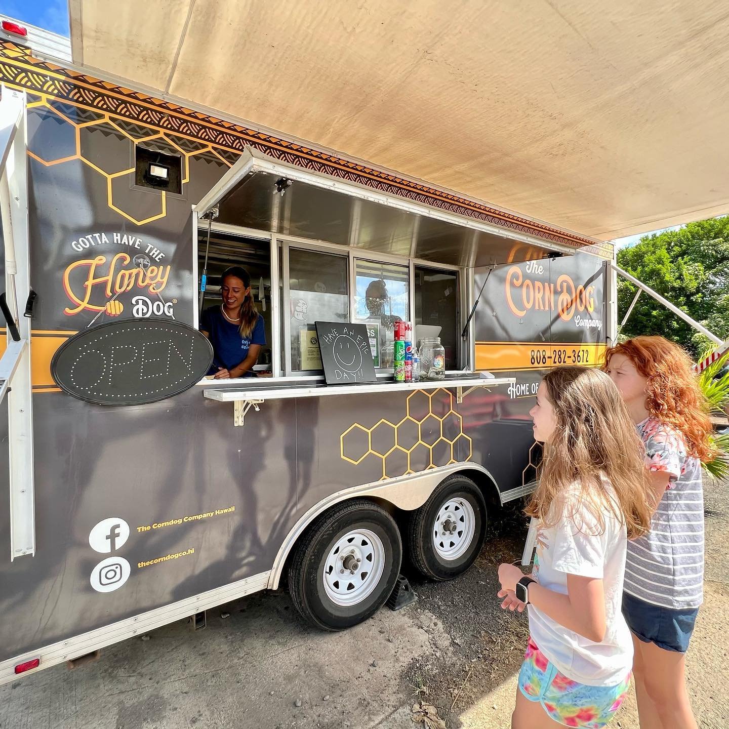 Kahuku Food Trucks A food truck with 'Hoggy Dog' branding and a 'Cornbox' banner serves customers under a shade structure.