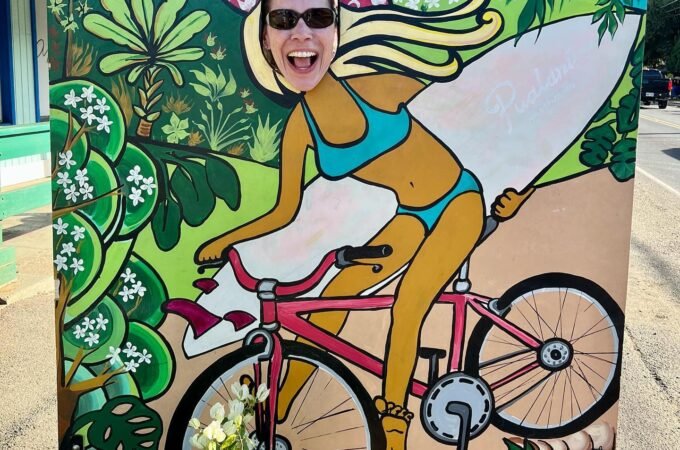 A colorful face board depicts a cyclist surfing through a tropical landscape.