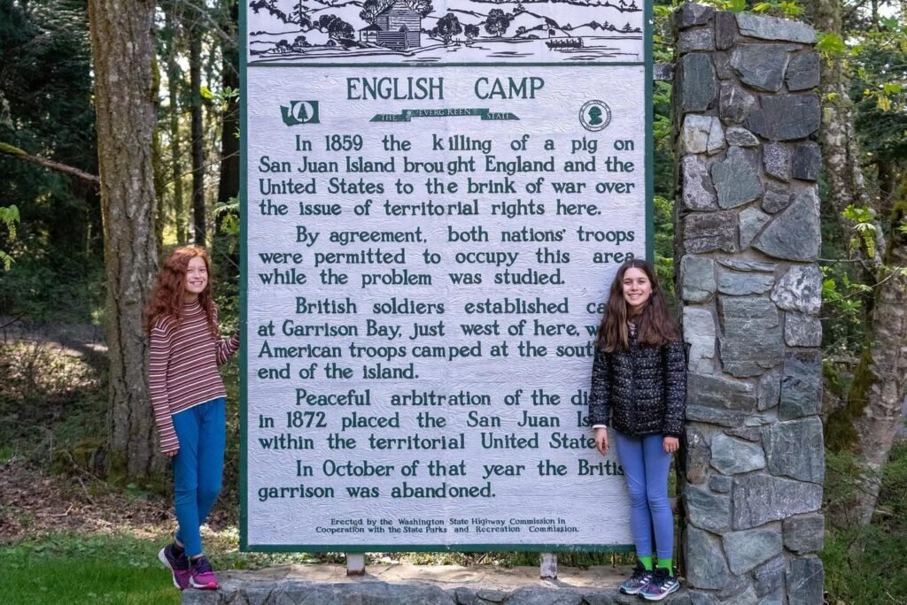 A child standing by the English Camp historical sign among the trees on Vancouver Island.