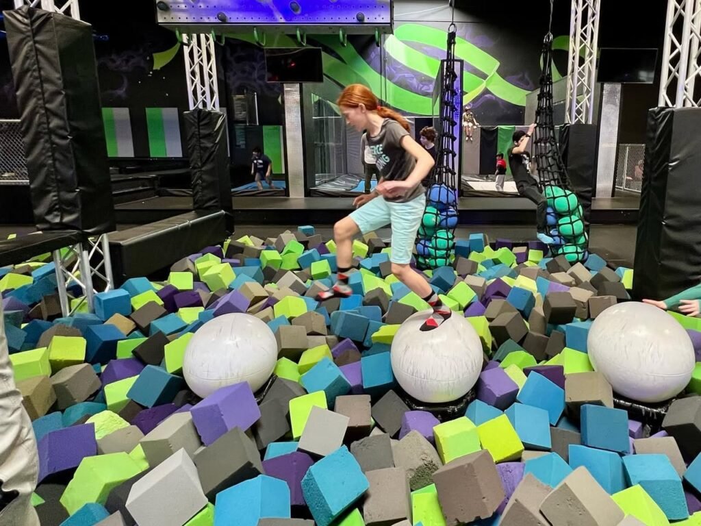 A person steps on white balance balls while standing in a foam pit filled with multicolored cubes.
