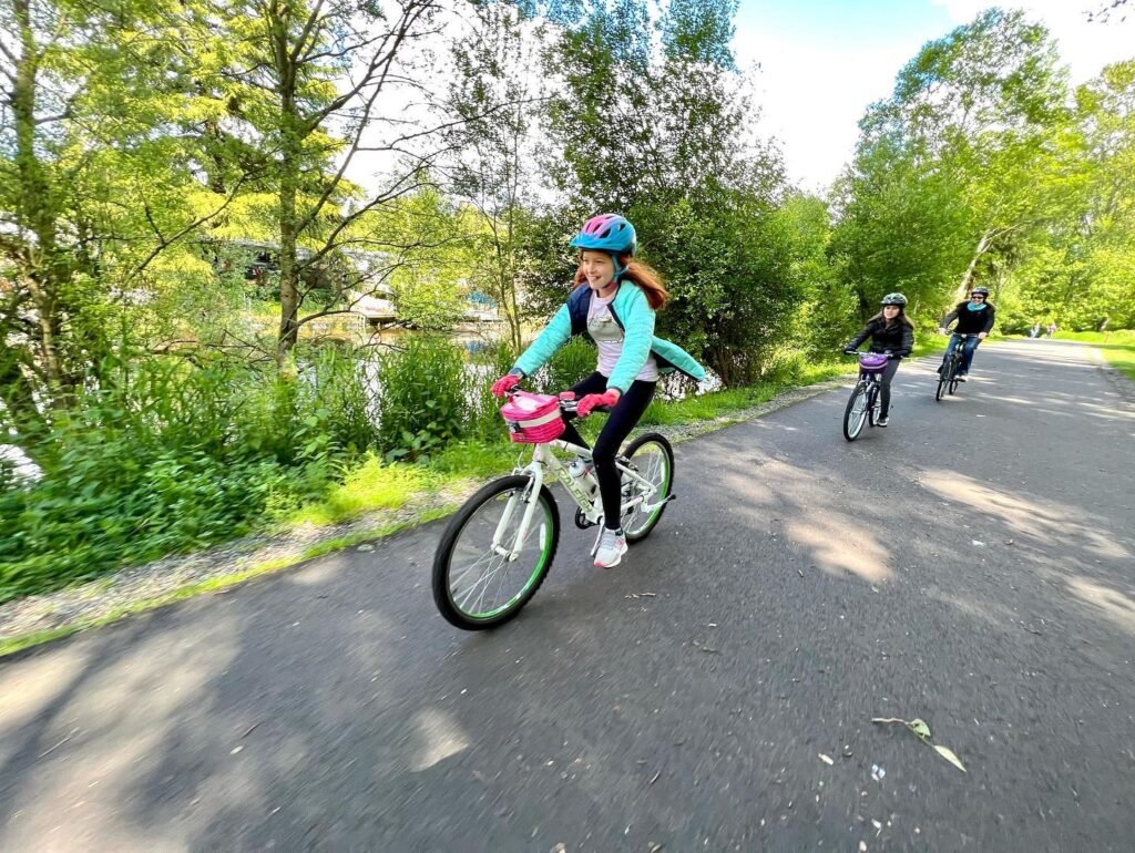 Riders enjoy a peaceful bike ride on a tree-lined paved path during a sunny day.