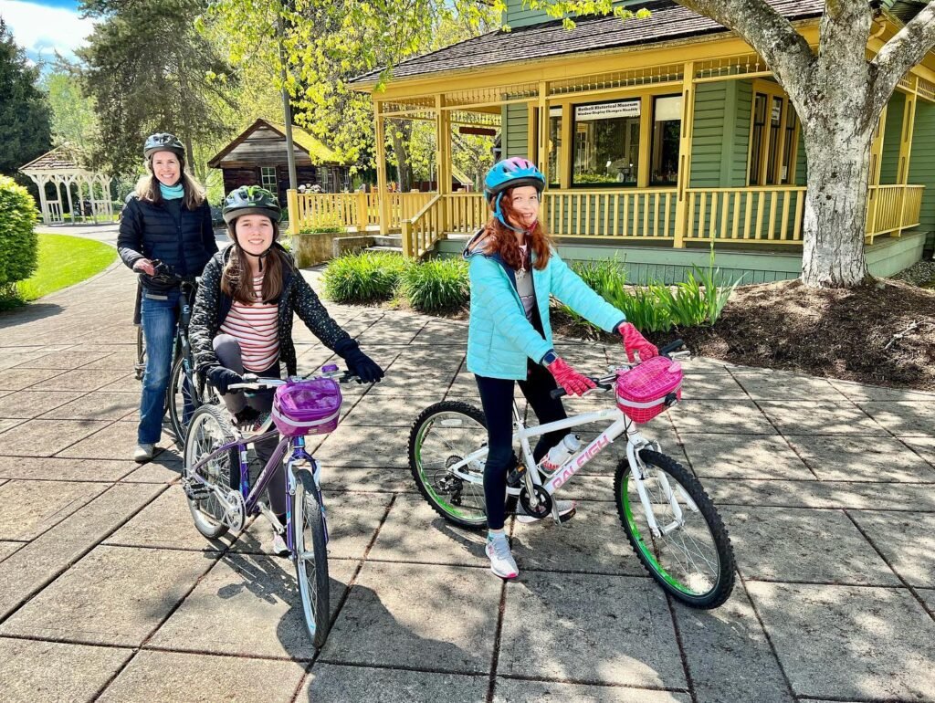 Two girls on bicycles and one adult ride through The Enchanted Forest in Pacific Grove, California.