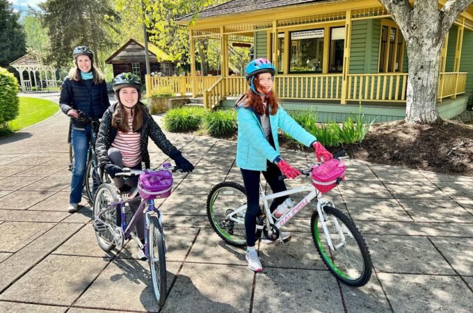 Two girls on bicycles and one adult ride through The Enchanted Forest in Pacific Grove, California.