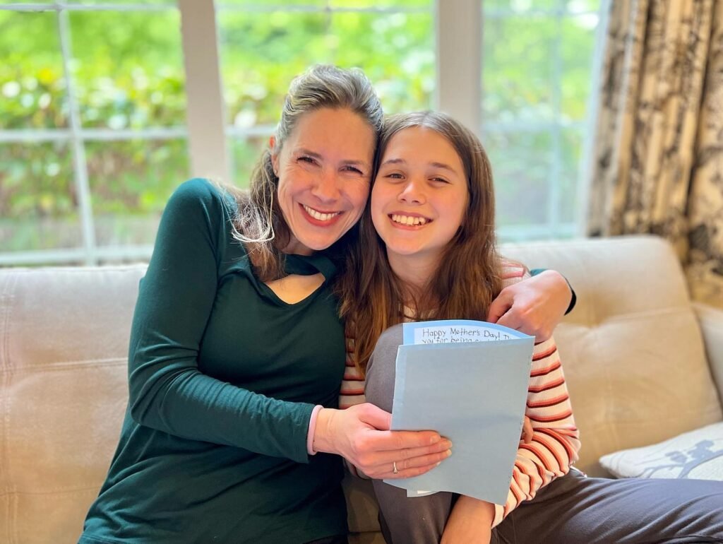 Two people smiling on a couch while holding a book during a sunny day.
