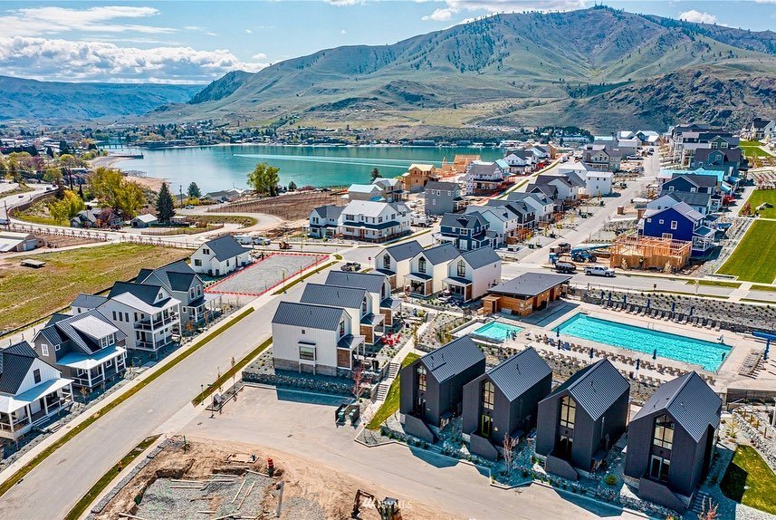 An aerial view of the Lindis Lake development in Dunedin, New Zealand, featuring modern homes, a resort with a turquoise pool, and the lake surrounded by rolling hills.