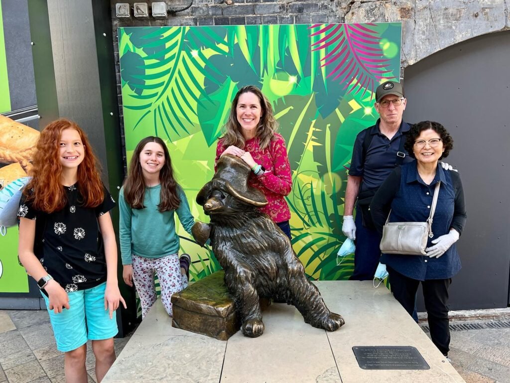 A group of visitors poses happily next to a bronze bear statue in front of a colorful tropical mural.