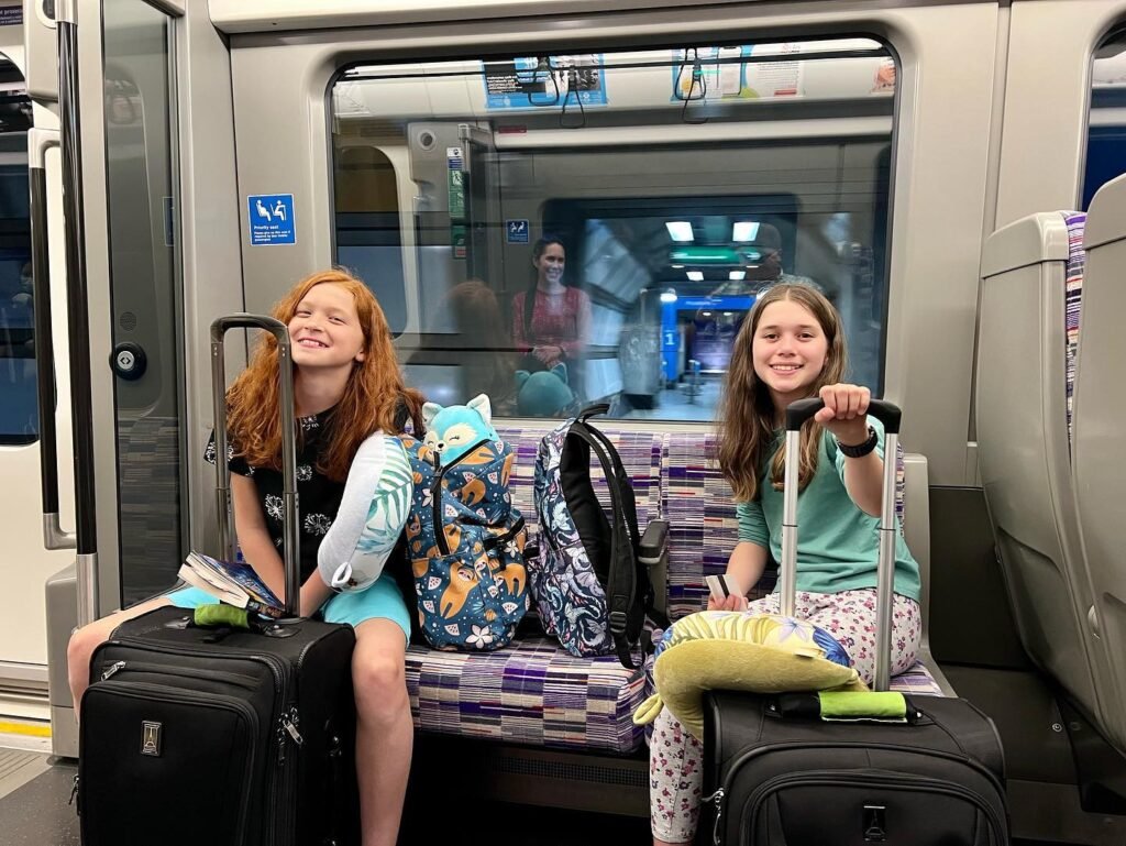 Two travelers with luggage and a turtle backpack sitting on a train.