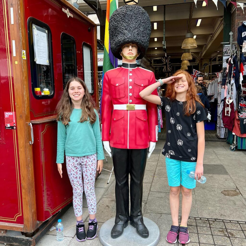 Two people posing beside a vintage-style mannequin dressed in a red royal guard uniform and bearskin hat, standing next to a red train car.