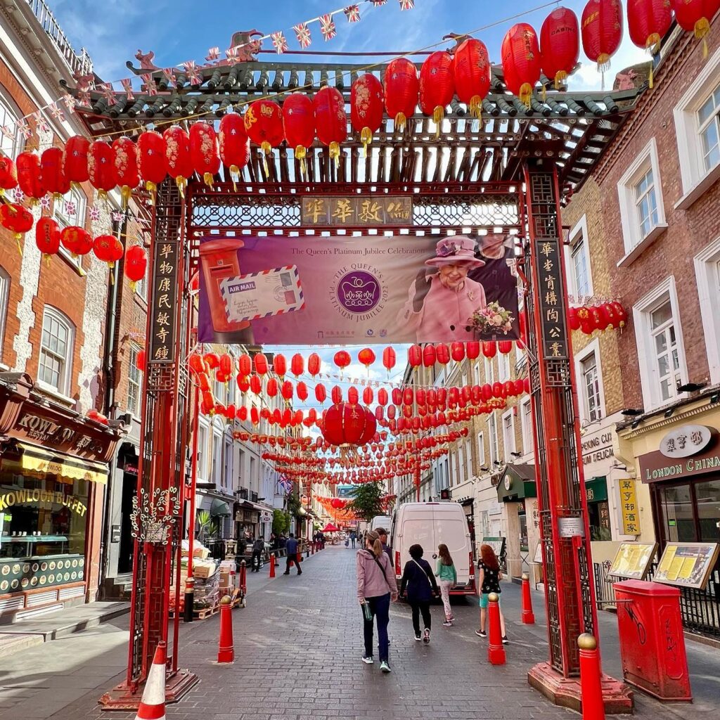 A pedestrian street lined with red brick buildings and decorated with dozens of hanging red paper lanterns. Visitors stroll beneath ornate traditional gates and festive canopies.