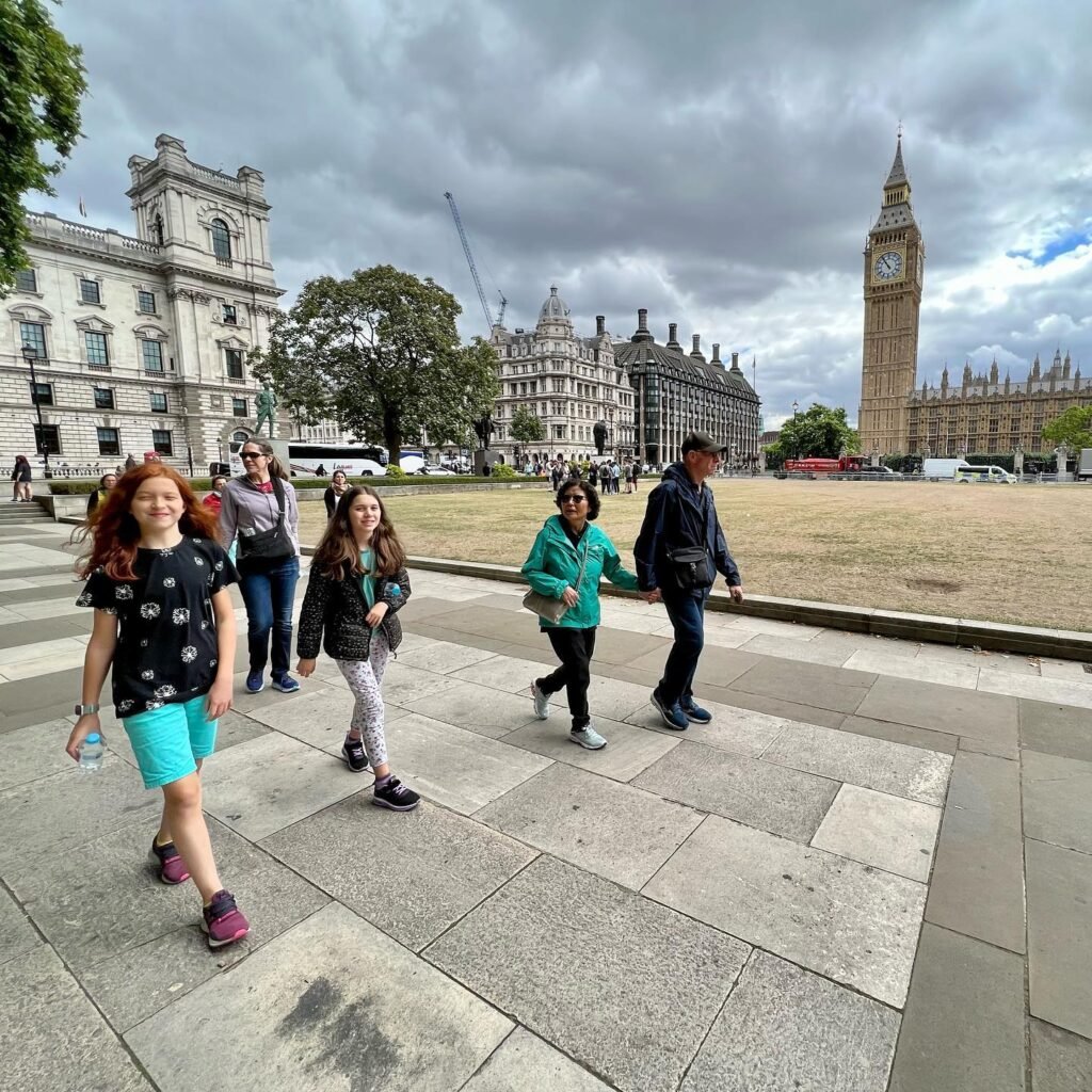 A group of people stroll around London's Parliament Square with Big Ben in the background under a cloudy sky.