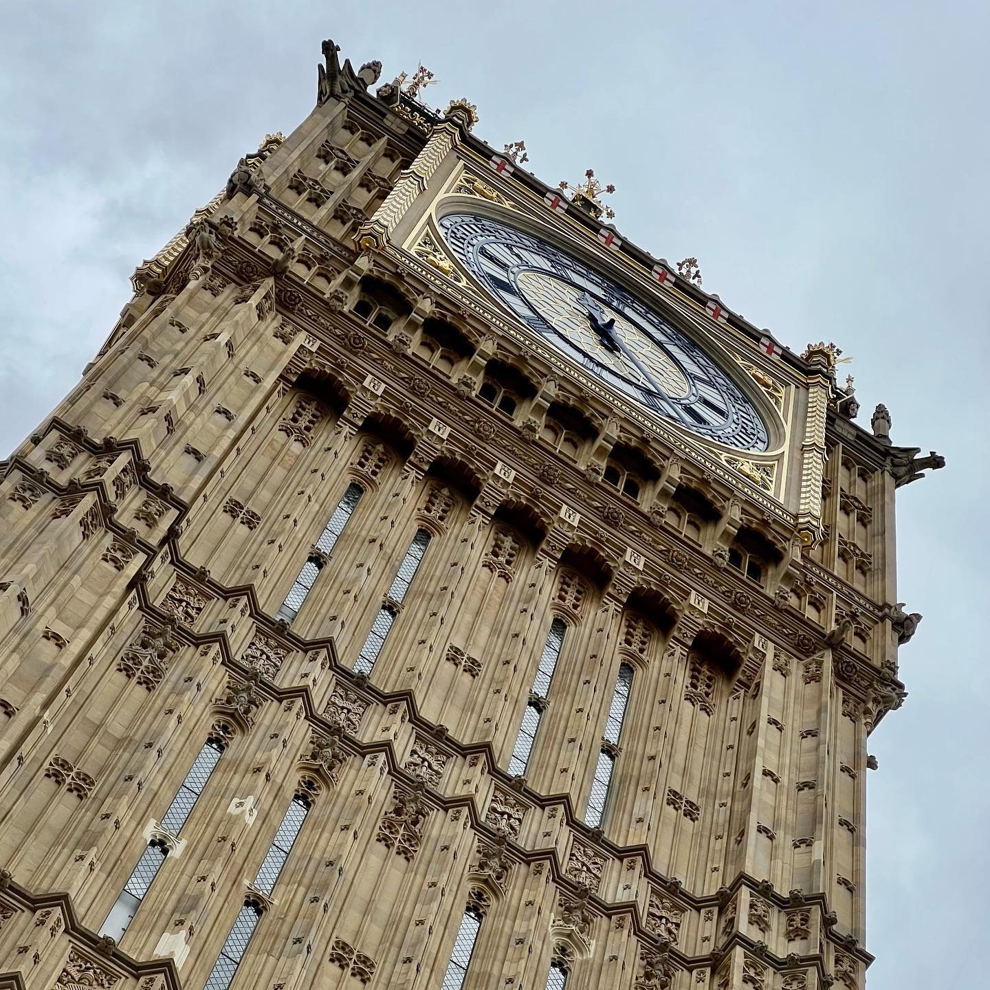 Trafalgar Square to Westminster Abbey Upward angle of an ornate stone clock tower, highlighting the clock face and architectural details against the sky.