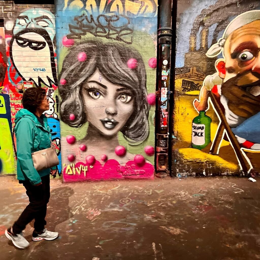Colorful graffiti featuring a detailed face and abstract figures. A person walks past vibrant urban street art.