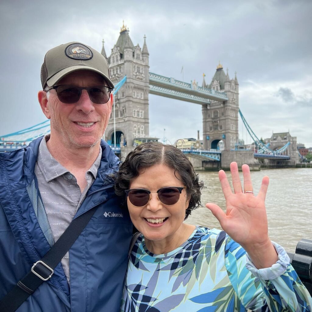Two travelers pose in front of London's iconic Tower Bridge during a sunny day.