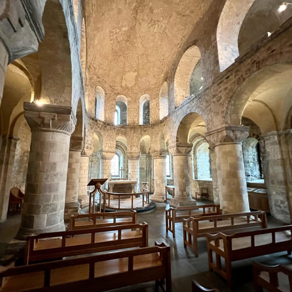 Interior of a historic stone church featuring arched ceilings, wooden pews, and classical columns.