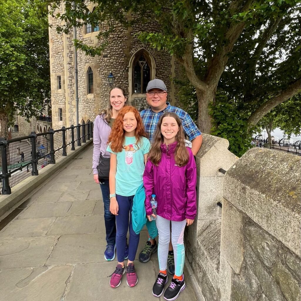 A family stands together on a stone bridge with a historic castle and trees in the background. The smiling group poses for a photo during a travel experience.