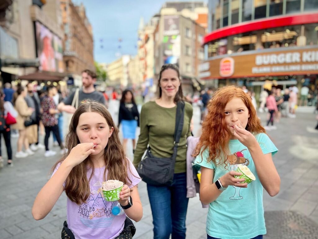 A family enjoying street ice cream on a busy street featuring a Burger King and stone architecture.