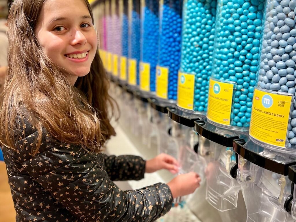 A happy person uses a dispenser to pick a bag of assorted blue M&Ms.
