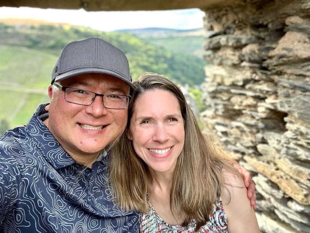 A couple sharing a selfie near a rough stone structure with rolling green hills in the background.