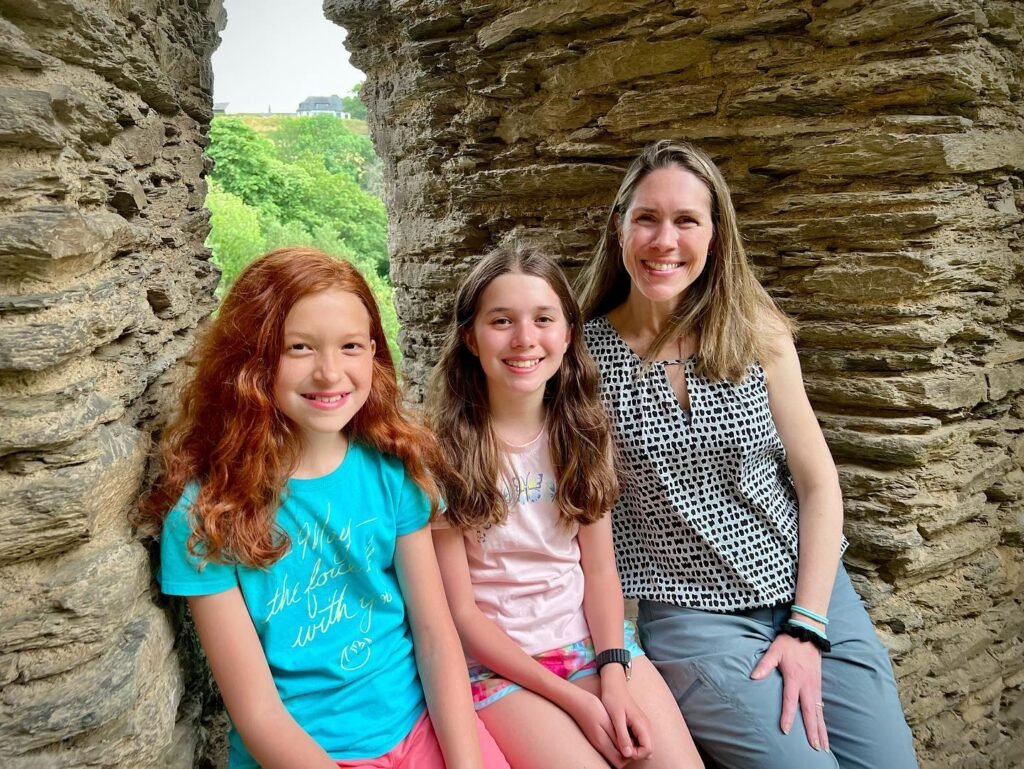 Three people sitting in a stone structure with lush greenery visible outside.
