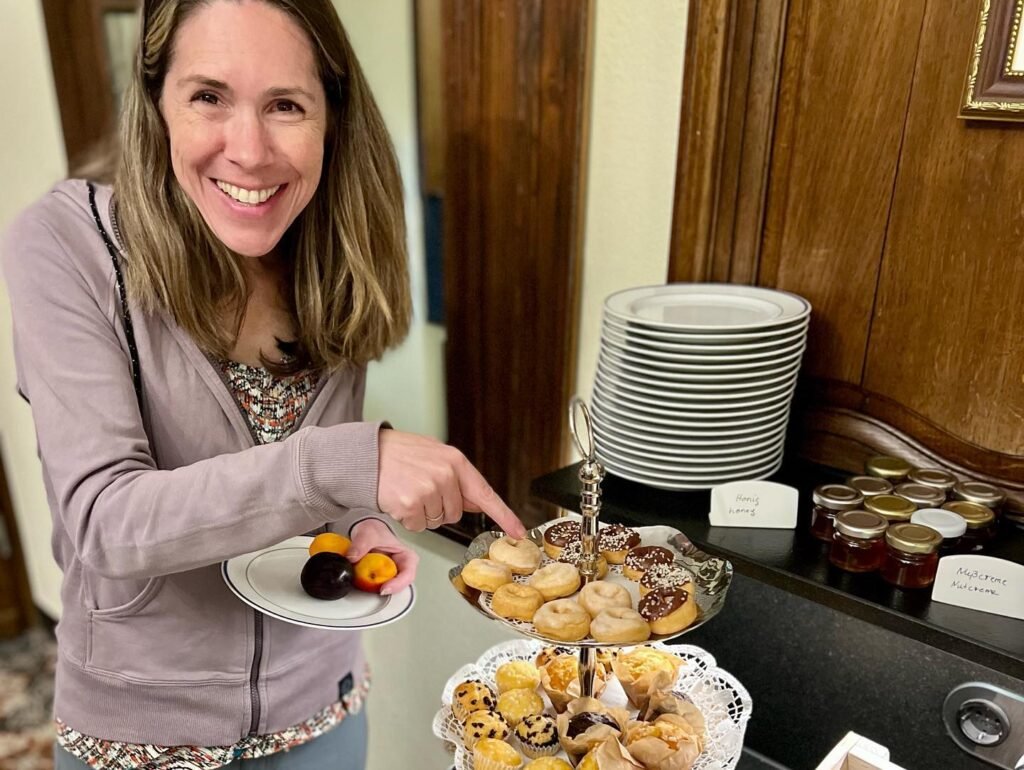 A woman selects pastries and chocolates from a tiered tray at a hospitality station.