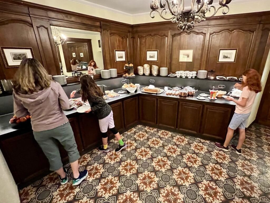 Guests select food from a buffet in a room featuring dark wood paneling and an ornate patterned floor.
