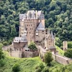 Bacharach A detailed view of a historic stone castle perched on a lush, green hillside surrounded by dense forest.