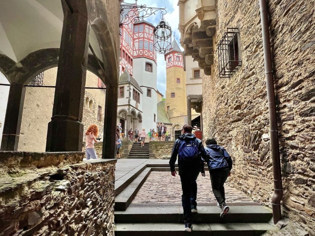 Two travelers walk down a historic stone alleyway with colorful towers in the background. A close-up view of stone arches and textured walls.