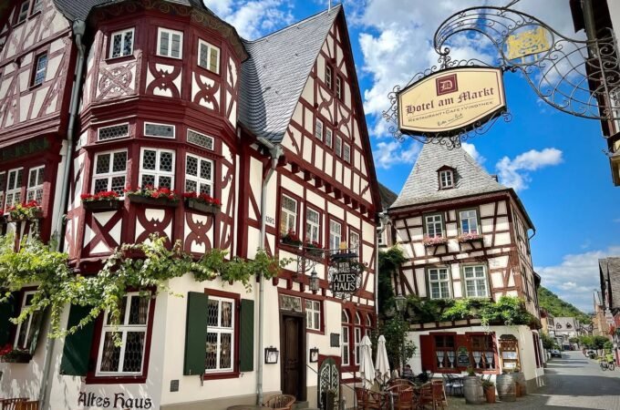 A collage of picturesque half-timbered houses with red and white facades and a traditional German-style hanging sign under a blue sky.