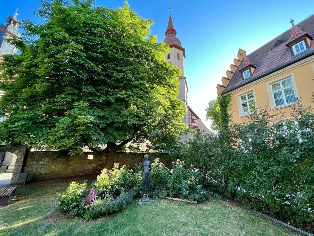 A serene castle courtyard garden featuring a stone tower, lush greenery, and a statue.
