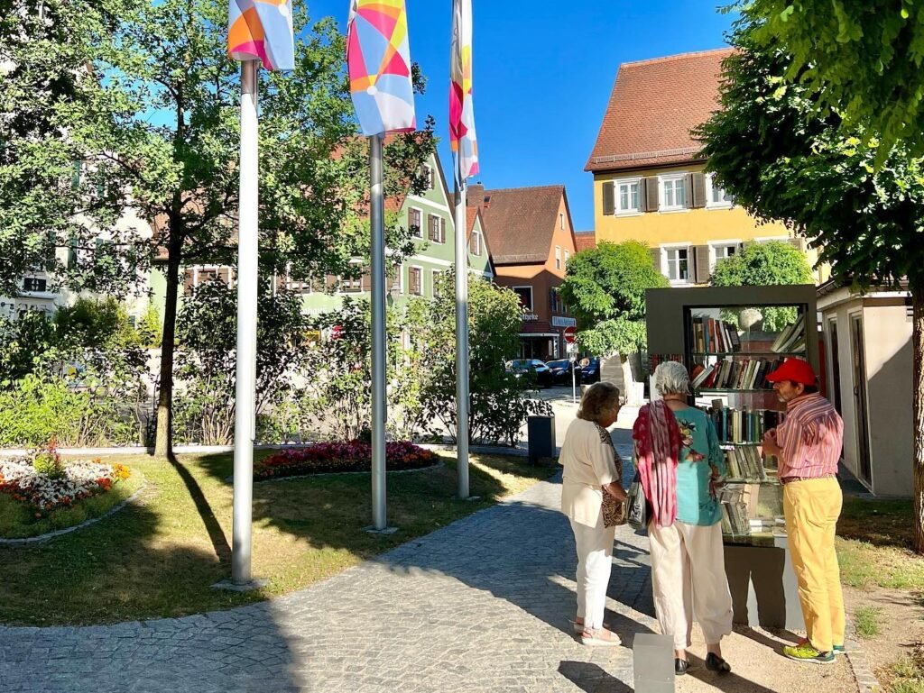 Bright penny flags on light poles and a group of four visitors standing in the distance of a colorful village plaza in Germany.