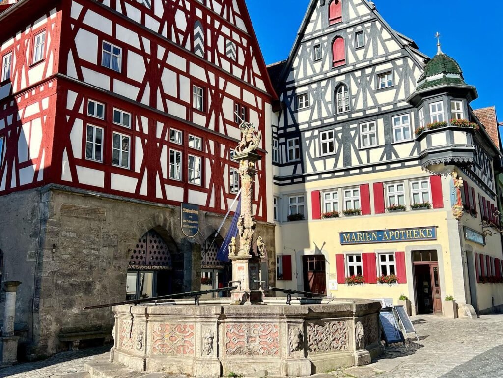 Traditional German half-timbered buildings with a historic fountain in a sunlit town square.
