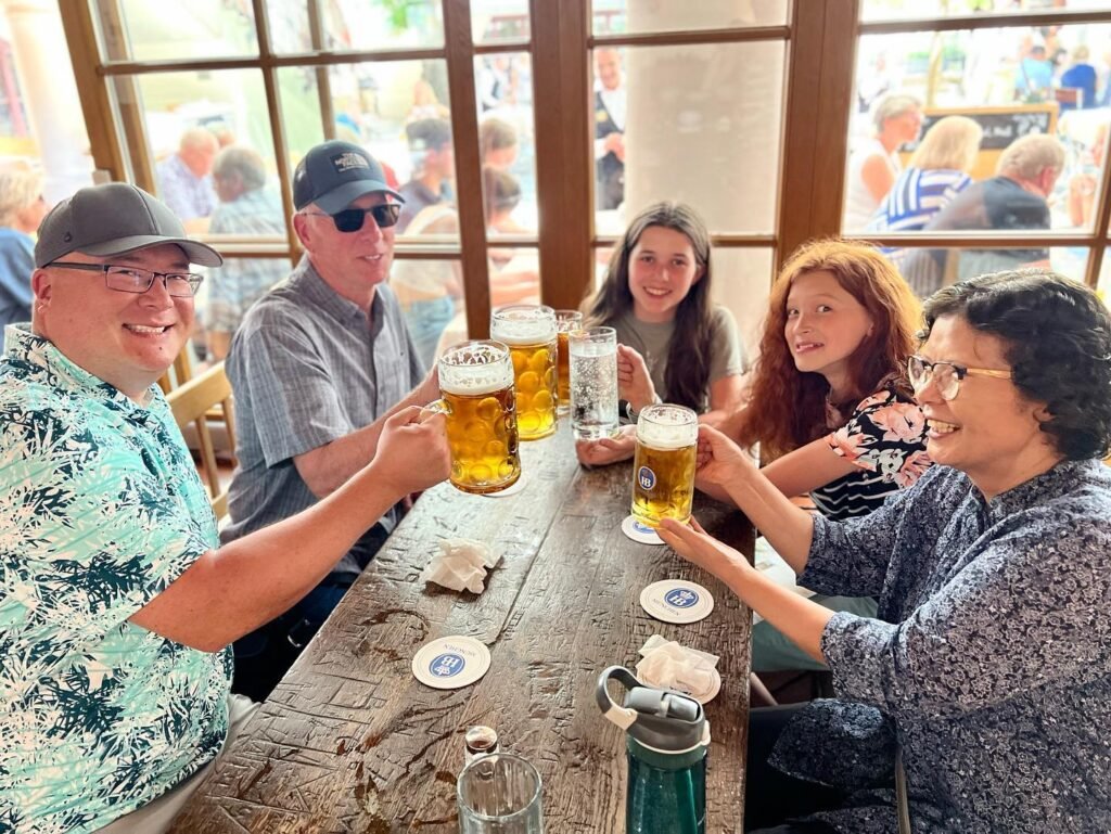 A group of people toasting with beer at a wooden table in a bright, social setting.