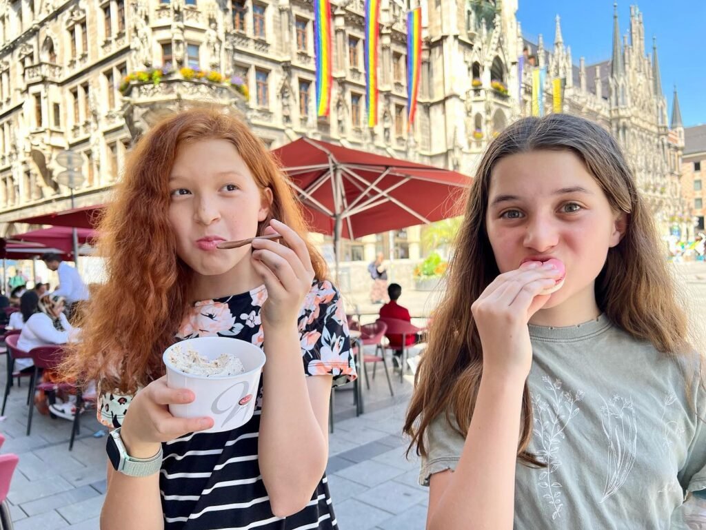 Two girls enjoy a pastry while seated near a historic cathedral.