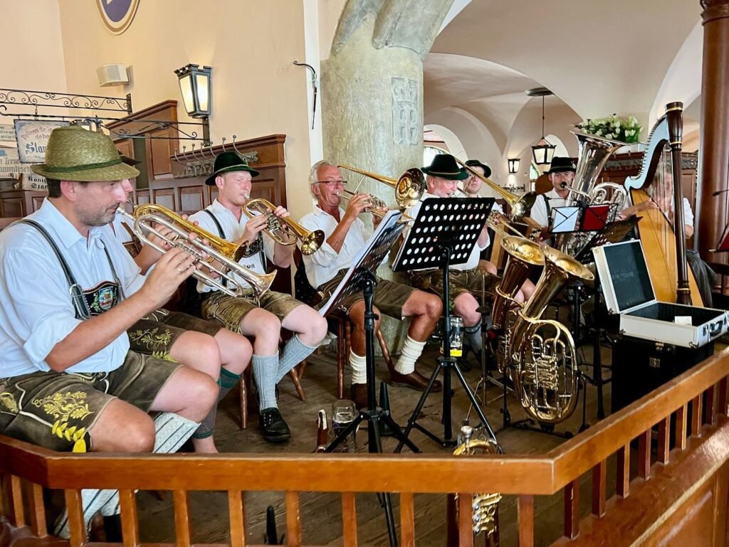 A group in traditional hats and suspenders plays brass instruments from an elevated wooden platform.