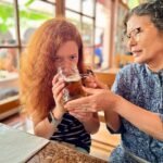 Dachau A person with reddish-orange hair sips a drink at a bar while another person stands nearby.