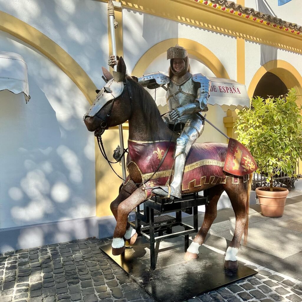 A detailed statue of a knight in full armor on a horse is displayed outside a restaurant with gold-trimmed arches. The figure holds a standard with the word 'ESPAÑA' clearly visible.