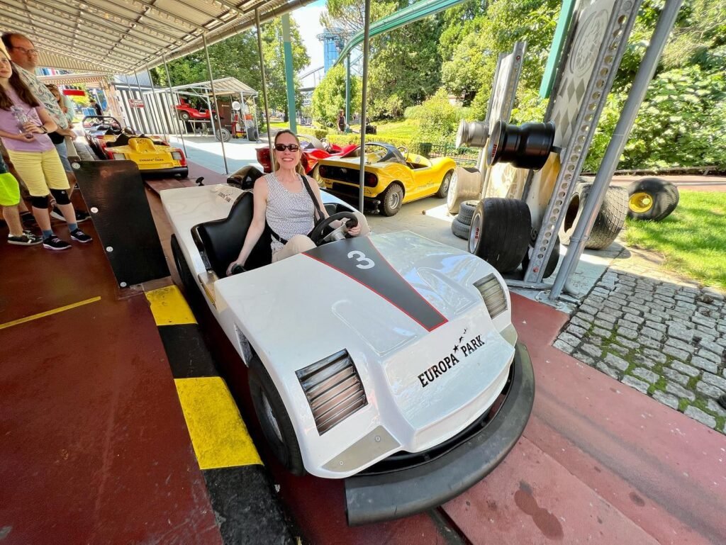 A person in a white go-kart at an amusement park attraction with other colorful karts in the background.