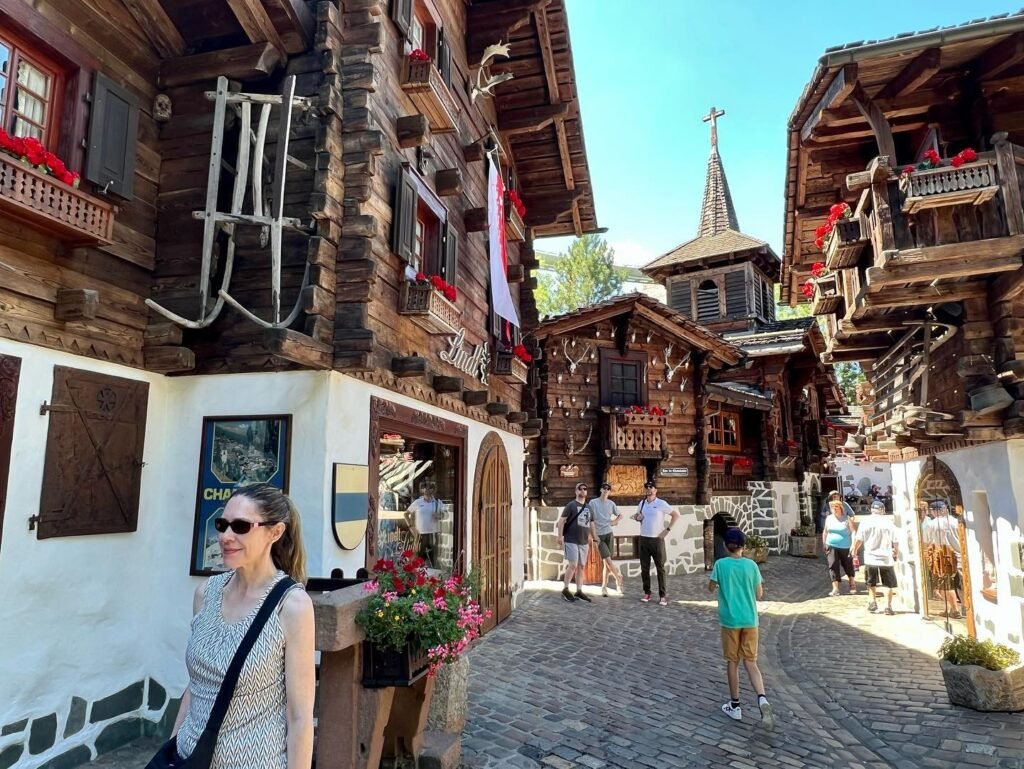 Visitors in a cobblestone courtyard of historical wooden buildings with a steeple in the background.