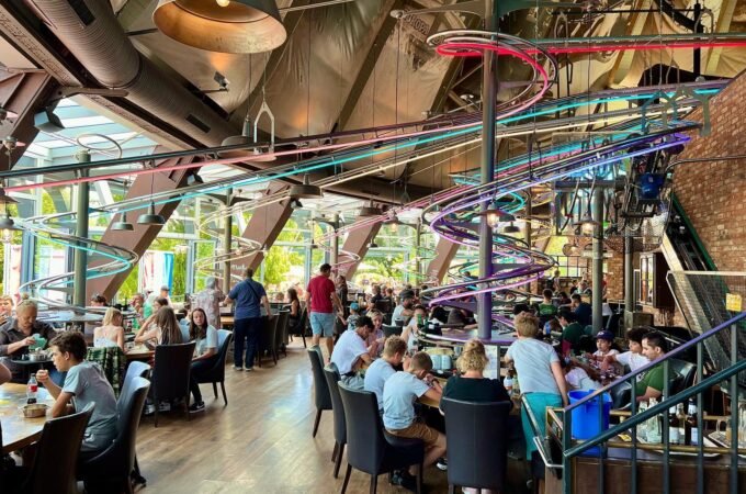 A bustling indoor dining area with colorful roller coaster tracks overhead