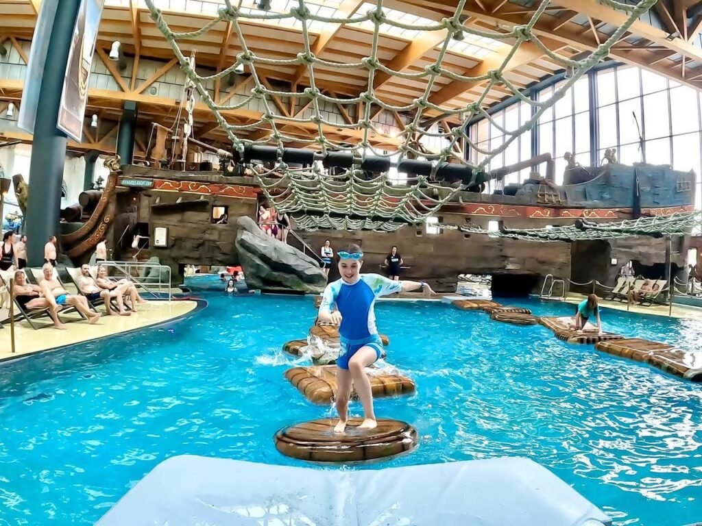A child balances on floating platforms in a large indoor water park pool beside an ark.