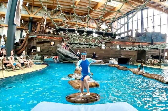 A child balances on floating platforms in a large indoor water park pool beside an ark.