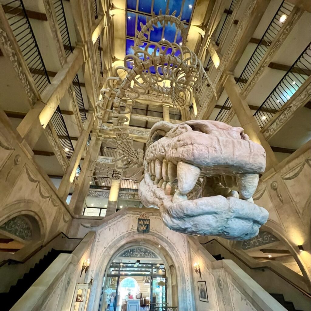 An elegant atrium features a grand chandelier and a massive stone gargoyle suspended from a high ceiling.