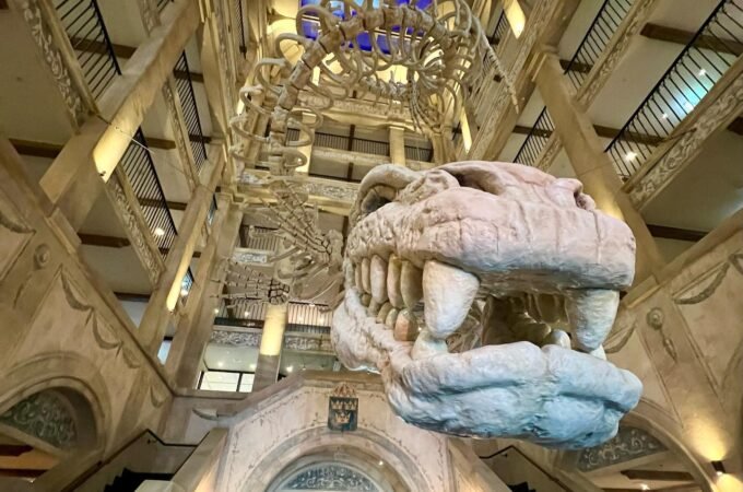 An elegant atrium features a grand chandelier and a massive stone gargoyle suspended from a high ceiling.