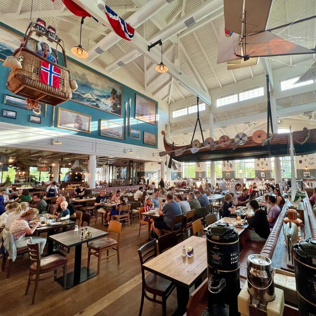 A bustling interior of a restaurant with maritime-themed decor, featuring a Viking boat, pennant flags, and a balsa wood hot-air balloon with Norwegian imagery.
