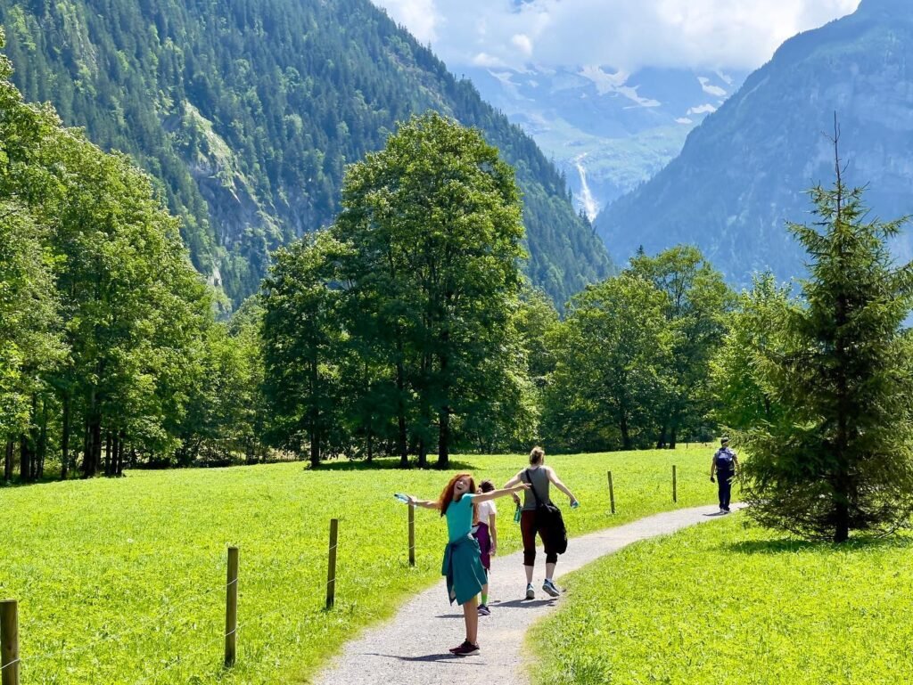 People exploring a scenic path surrounded by green grass, trees, and mountains in the Pacific Northwest.